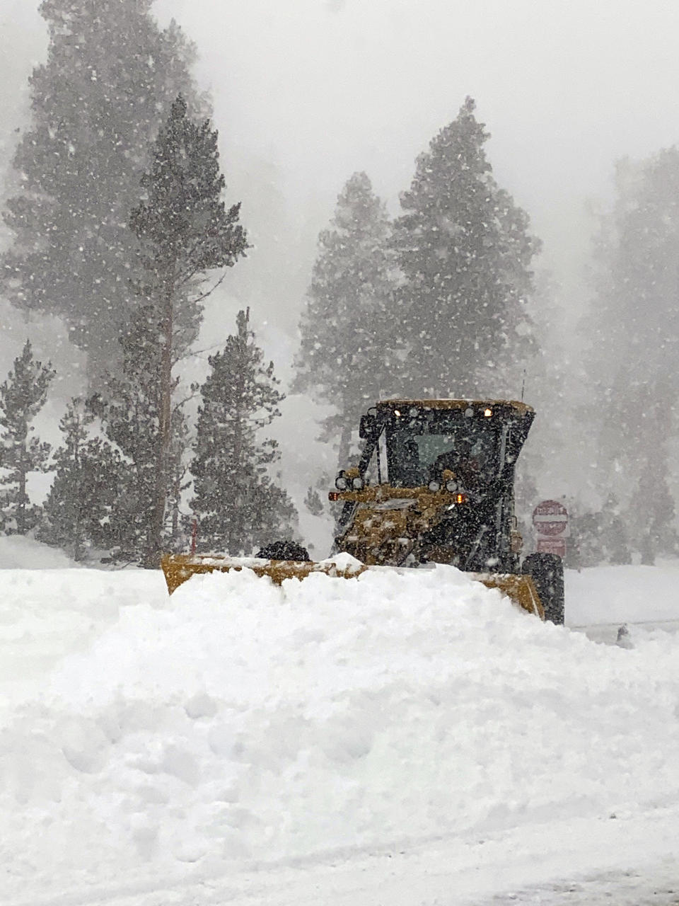 In this photo provided by Caltrans District 9, an earth mover clears heavy snow that fell along a closed U.S. Hwy 395, at Wilson Butte, in Mono County, Calif. on Wednesday, Jan. 27, 2021. An atmospheric river storm pumped drenching rains into the heart of California on Thursday as blizzard conditions buried the Sierra Nevada in snow. (Greg Miller/Caltrans District 9 via AP)