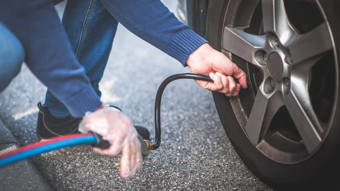 Man checking pressure and inflating car tire.