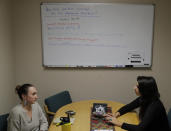 Caitlin Marie-Lieb Keller, left, and Sofia Locklear, right, both employees of the Urban Indian Health Institute in Seattle, have a meeting in front of a white board used for an earlier discussion of the federal government shutdown, Friday, Jan. 11, 2019, in Seattle. Fallout from the federal government shutdown is hurting hundreds of Native American tribes and entities that serve them. The pain is especially deep in tribal communities with high rates of poverty and unemployment, and where one person often supports an extended family. (AP Photo/Ted S. Warren)