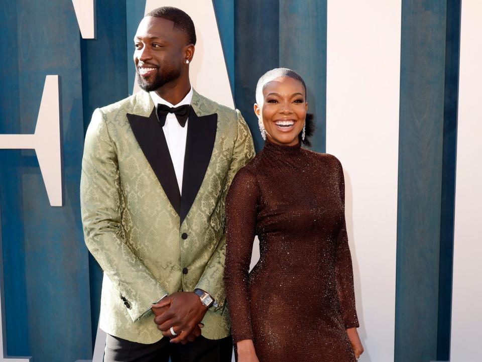 Dwayne in a mint green textured blazer with black lapels and a black bowtie and black pants. Gabrielle in a shimmering brown turtleneck long sleeve gown.