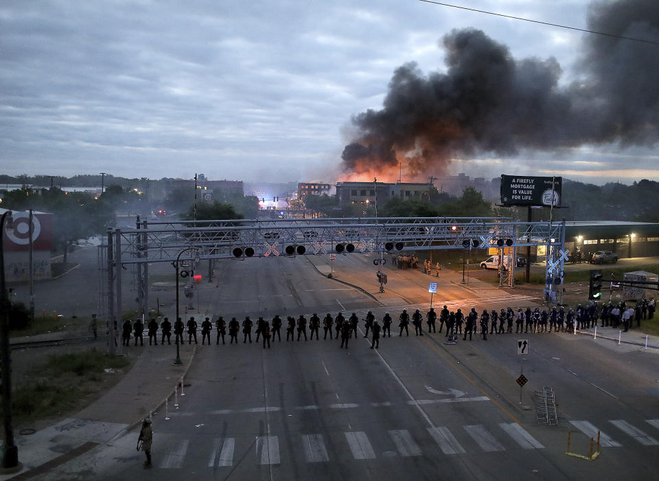 FILE - In this Friday, May 29, 2020 file photo, law enforcement officers stand in formation along Lake Street near Hiawatha Avenue as fires burned after a night of unrest and protests in the death of George Floyd in Minneapolis. Floyd died after being restrained by Minneapolis police officers on Memorial Day. (David Joles/Star Tribune via AP)