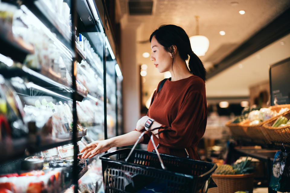 Side profile of beautiful young Asian woman carrying a shopping basket, grocery shopping for daily necessities in supermarket. Healthy eating lifestyle. Making healthier food choices