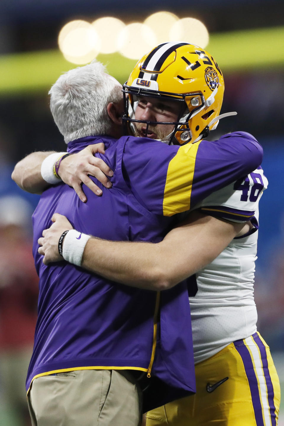 LSU Offensive Coordinator Steve Ensminger embracxes LSU long snapper Blake Ferguson (48) before the first half of the Peach Bowl NCAA semifinal college football playoff game between LSU and Oklahoma, Saturday, Dec. 28, 2019, in Atlanta. Ensminger's daughter-in-law, Carley McCord, died in a plane crash Saturday in Louisiana on the way to the game. (AP Photo/John Bazemore)