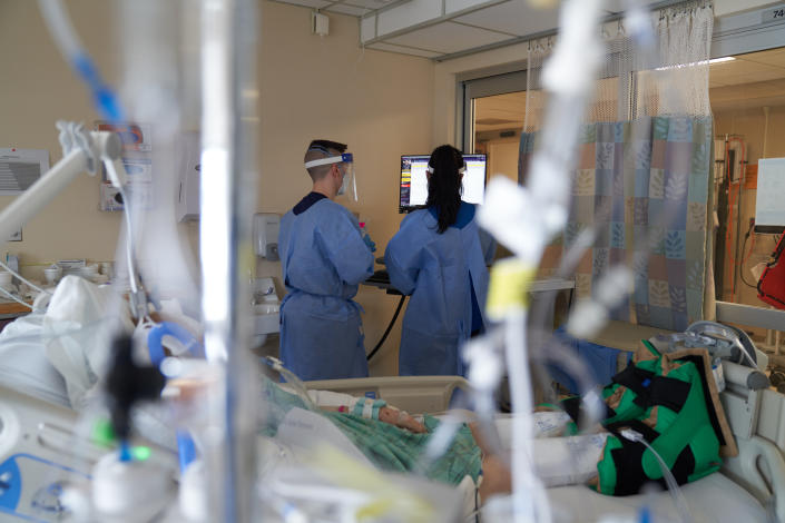 Health care workers look at a monitor as they treat a Covid-19 patient in a hospital room. 