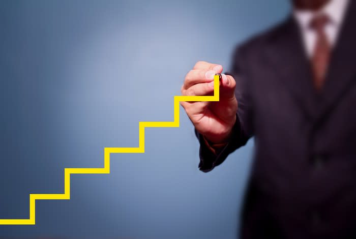 A man in a suit drawing an ascending yellow step chart.