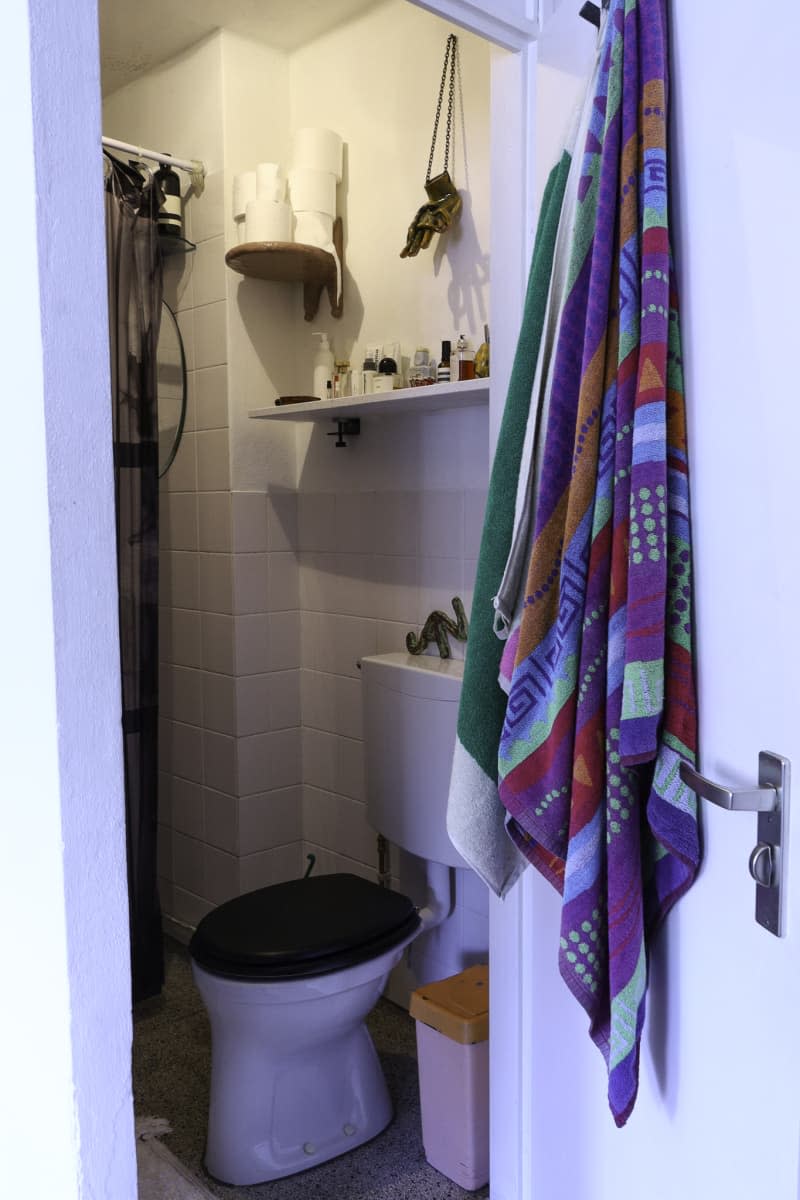 View into white tile bathroom with colorful towels hanging on door