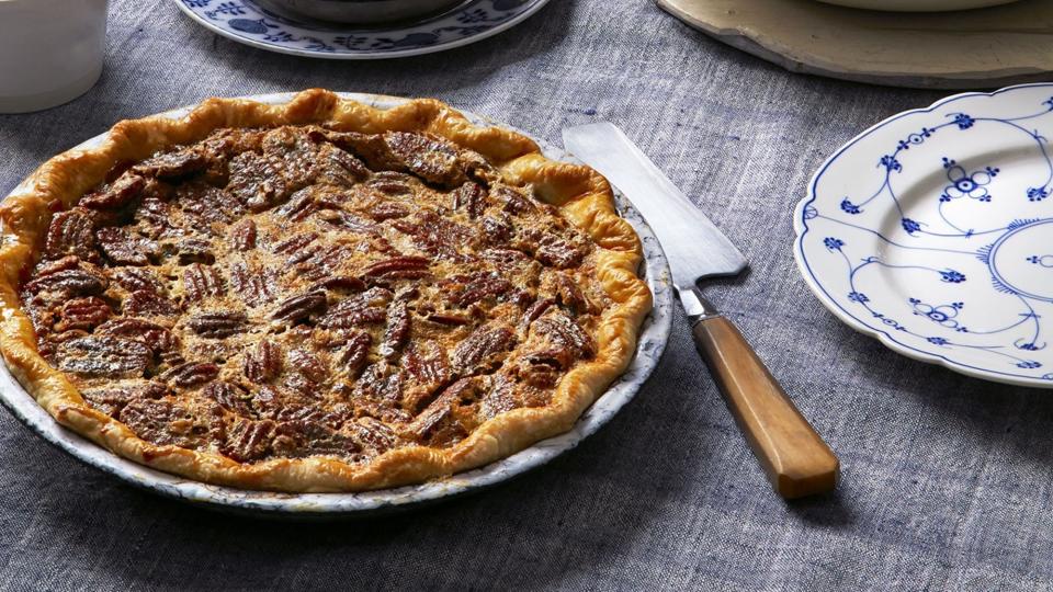 boozy pecan pie with a pie server and a bowl of whipped cream for serving