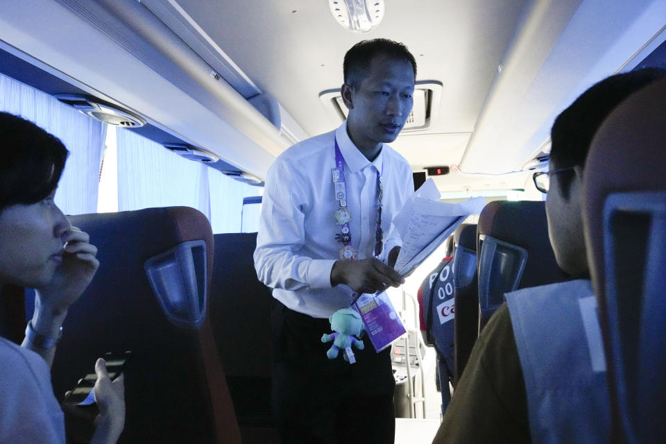 A Chinese volunteer talks to reporters to inform them about it's departure time at a shuttle bus hub at the 19th Asian Games in Hangzhou, China, Tuesday, Sept. 26, 2023. Signs around Hangzhou billed the city as a "paradise on earth" while China adopted the motto "heart to heart" for the games, which attract feature some 12,000 competitors, more than the summer Olympics, from across Asia and the Middle East. (AP Photo/Aaron Favila)