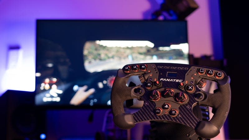 A Fanatec sim racing wheel, mounted on a desk in front of a computer screen.  It is bathed in neon purple bisexual lighting