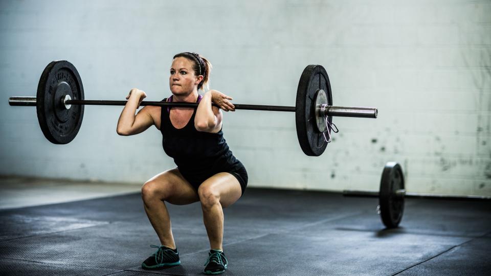 Woman at the bottom of a squat, wearing workout clothes and flat shoes with barbell resting at the front of her shoulders