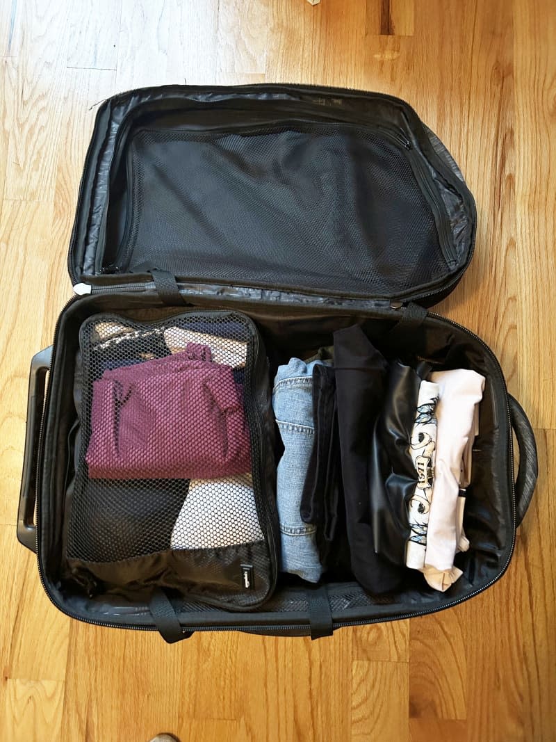 Suitcase on floor packed with rolled clothes and mesh bag