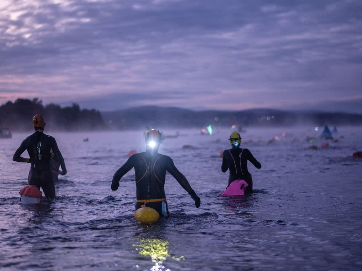 Wearing headlamps, CanadaMan/Woman participants enter Lac Mégantic in a staggered start to the race on Oct. 3, 2021. The swim had to be shortened to 1.5 kilometres because the water was just 12 C. (Michel Caron/Endurance Aventure - image credit)