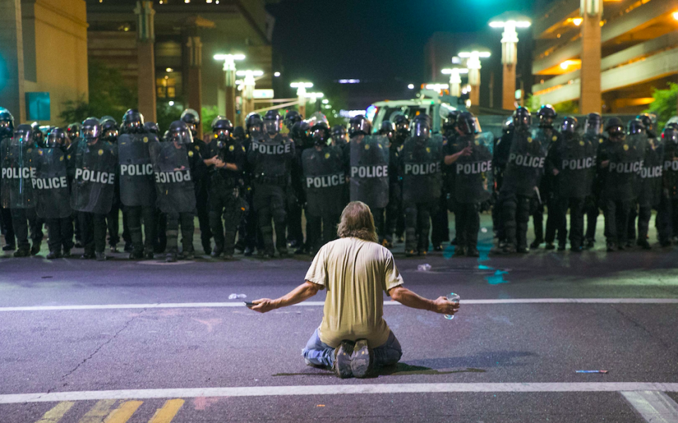 An anti-Trump protester sits in front of riot police outside the conference centre (Picture: Rex)