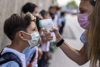 FILE - A teacher wearing a face mask to protect against the spread of coronavirus checks the temperature of her student at Maestro Padilla school as the new school year begins, in Madrid, Sept. 7, 2021. With one of Europe's highest vaccination rates and its most pandemic-battered economies, the Spanish government is laying the groundwork to approach the virus in much the same way countries deal with flu or measles. (AP Photo/Manu Fernandez, File)