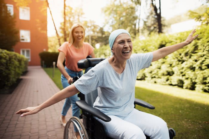 A woman sitting in a wheelchair, smiling with her arms outstretched.