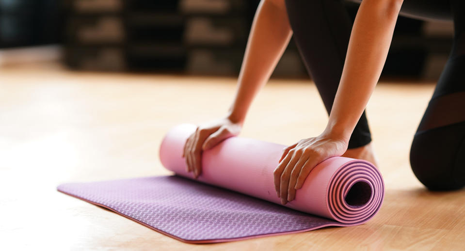Young woman folding yoga mat  after class end