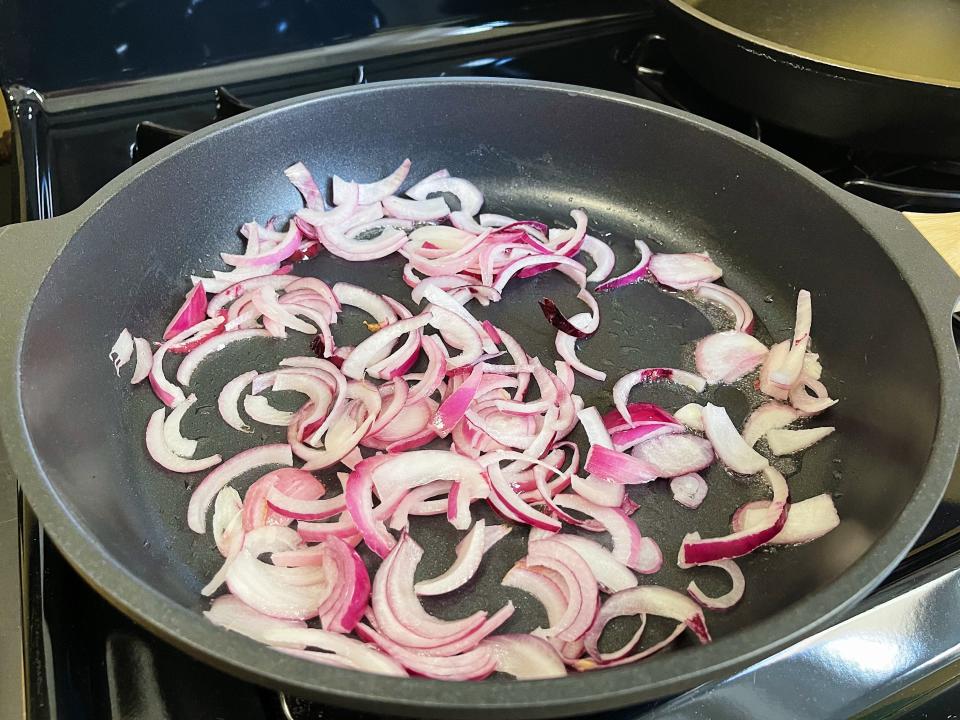 red onion slices cooking in a black pan