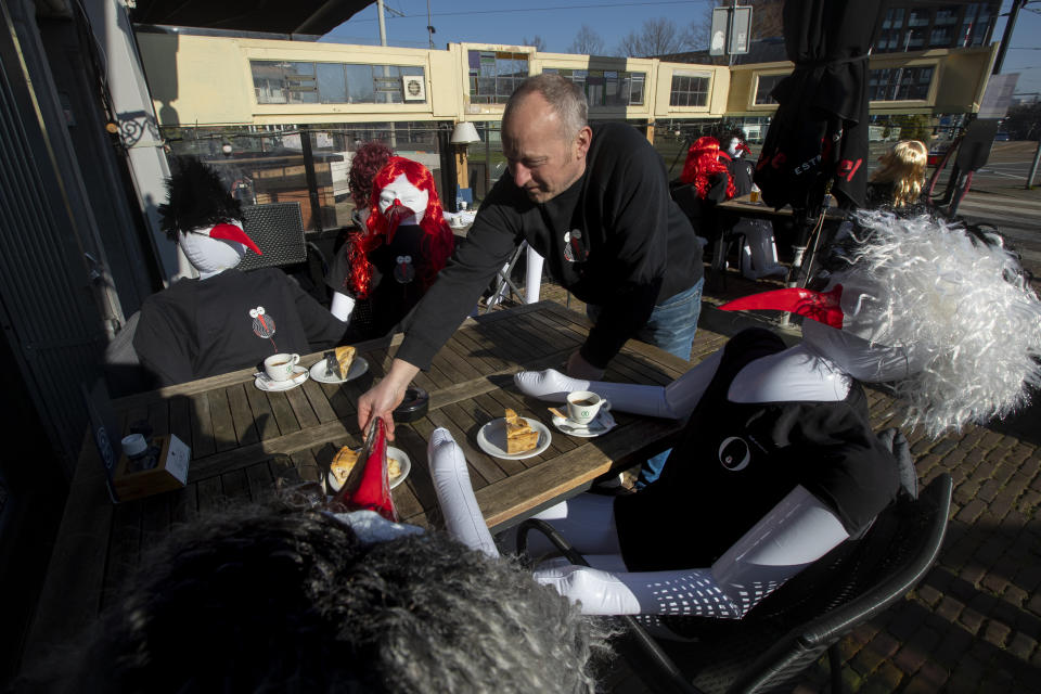 Cafe owner Peter Bender serves a piece of pie on his terrace filled with inflatable dolls at cafe De Ooivaar in Delfshaven, Rotterdam, Netherlands, Tuesday, March 2, 2021. Stores in one village opened briefly, cafe owners across the Netherlands were putting tables and chairs on their outdoor terraces and sex workers were planning a demonstration outside parliament in protests against the government's tough coronavirus lockdown. (AP Photo/Peter Dejong)