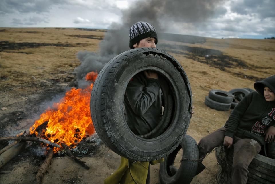 In this photo taken on Sunday, March 10, 2019, a boy holds a tire, during a ritual marking the upcoming Clean Monday, the beginning of the Great Lent, 40 days ahead of Orthodox Easter, on the hills surrounding the village of Poplaca, in central Romania's Transylvania region. Romanian villagers burn piles of used tires then spin them in the Transylvanian hills in a ritual they believe will ward off evil spirits as they begin a period of 40 days of abstention, when Orthodox Christians cut out meat, fish, eggs, and dairy. (AP Photo/Vadim Ghirda)