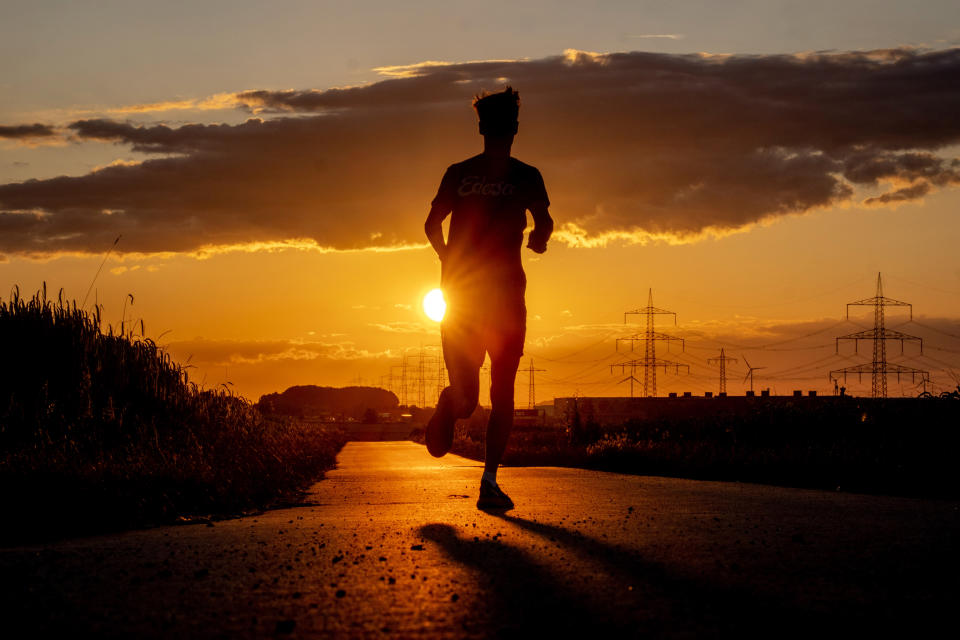 A man runs along a small road in the outskirts of Frankfurt, Germany, as the sun rises early Thursday, July 13, 2023. (AP Photo/Michael Probst)