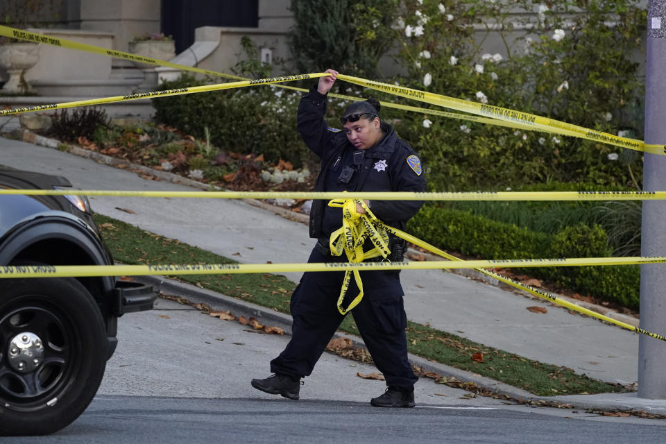 A police officer rolls out yellow tape on the closed street below the home of Paul and Nancy Pelosi in San Francisco, on Oct. 28, 2022. (Eric Risberg / AP)