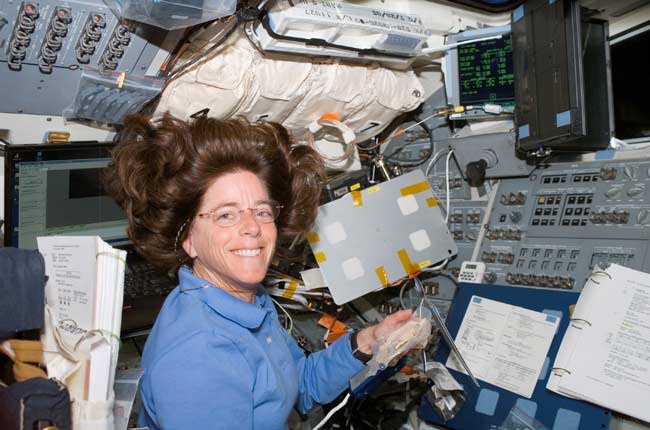 Barbara Morgan smiles at the camera while surrounded by various papers and equipment.