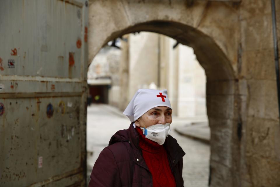 A nun wears a mask to help prevent the spread of the coronavirus next to the closed Church of the Holy Sepulchre, a place where Christians believe Jesus Christ was buried as a palm hangs on the door in Jerusalem's old city, Sunday, April 5, 2020. The traditional Palm Sunday procession was canceled due to restrictions imposed to contain the spread of coronavirus. (AP Photo/Ariel Schalit)
