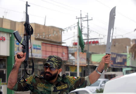 A Shi'ite fighter from Saraya al-Salam, who are loyal to radical cleric Muqtada al-Sadr, waves weapon in the back of a vehicle as he leaves from the holy city of Najaf in a convoy of vehicles heading to the northern Iraqi city of Tikrit to continue the offensive against Islamic State militants March 20, 2015. REUTERS/Alaa Al-Marjani