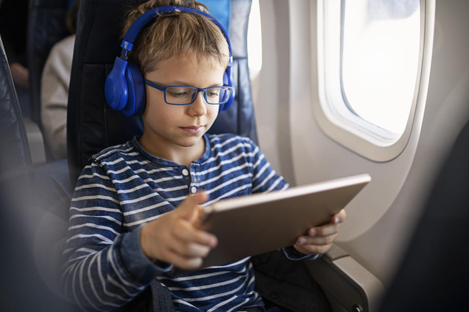 Little boy travelling by plane. The boy is using modern tablet and wireless headphones.
Nikon D850