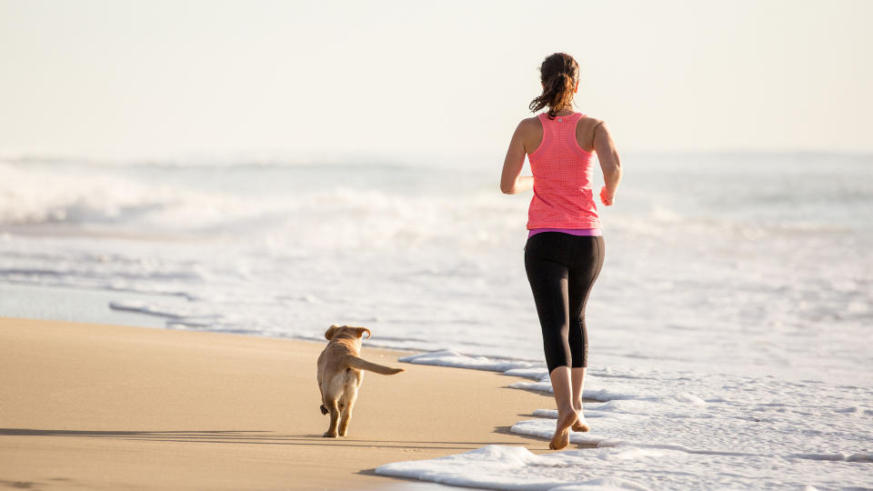 Lady running on beach with yellow Labrador