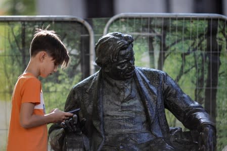 Radu Matei, 9 years old, looks at his phone next to the statue of George Enescu before attending a walking tour of Bucharest's hidden places