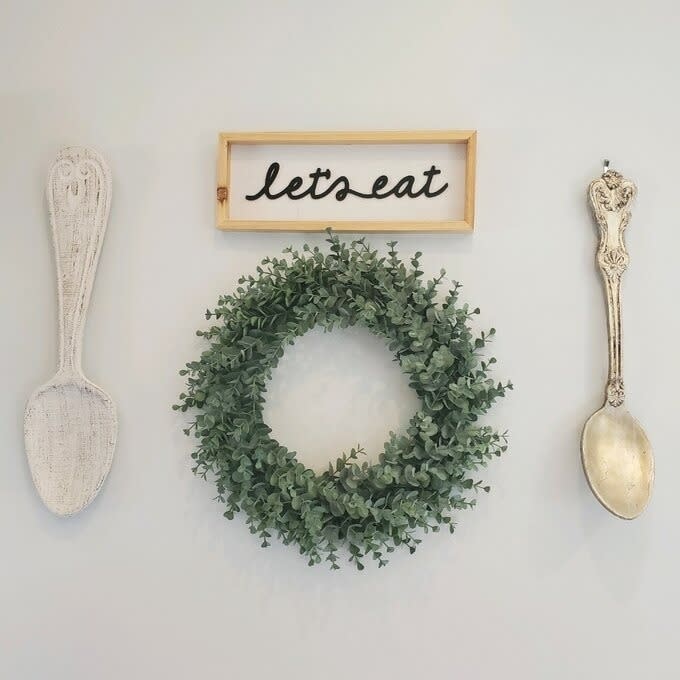 The wreath hanging under a sign that says "let's eat" and two spoon decorations on either side