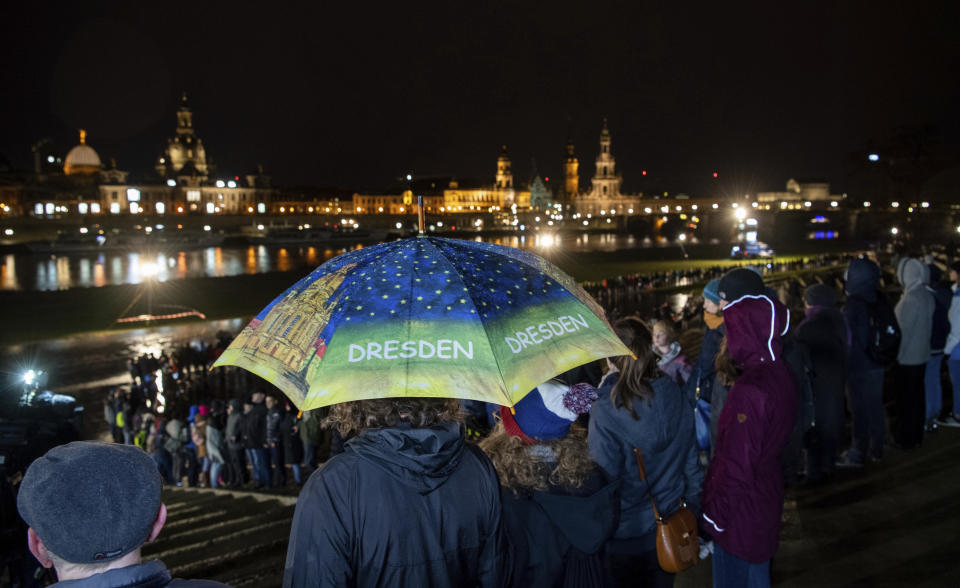 People form a human chain on the banks of the Elbe river with the historical old town in background, marking the 75th anniversary of the destruction of Dresden in the Second World War, in Dresden, Germany, Thursday Feb. 13, 2020. A 1945 allied bombing campaign reduced the centre of Dresden to rubble leaving about 25,000 people dead. (Robert Michael/dpa via AP)