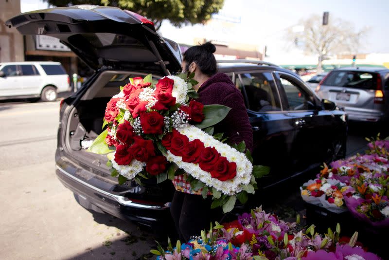 A woman lifts a funeral display into a car in the flower district in Los Angeles