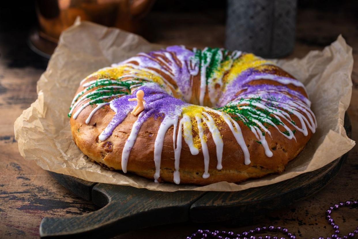mardi gras king cake decorated with white icing, green purple and gold sugar on parchment paper on rustic cutting board