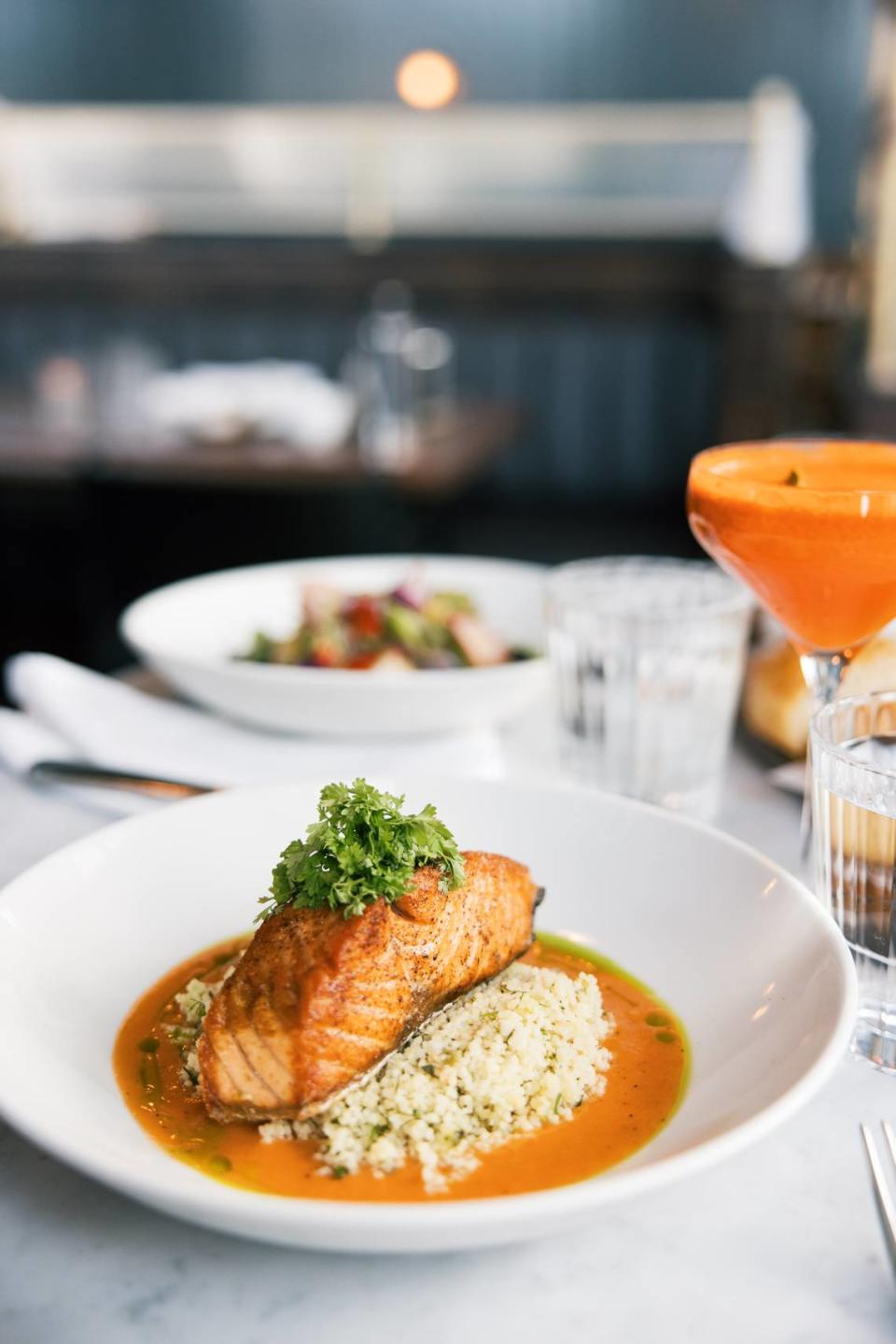 Entrees include Seared Salmon ($33) with lemon herb couscous, smoked tomato vinaigrette and chive oil. The cocktail is a Hindsight ($12, Tito’s vodka, house-pressed carrot juice, kaffir lime, and Thai basil).