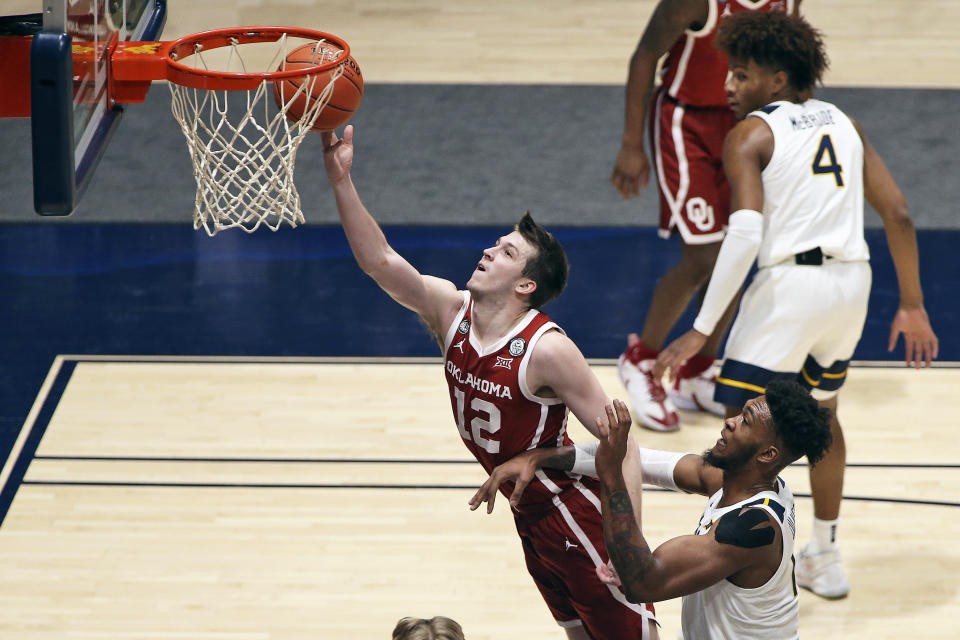 Oklahoma guard Austin Reaves (12) shoots past West Virginia forward Derek Culver (1) during the second half of an NCAA college basketball game Saturday, Feb. 13, 2021, in Morgantown, W.Va. (AP Photo/Kathleen Batten)