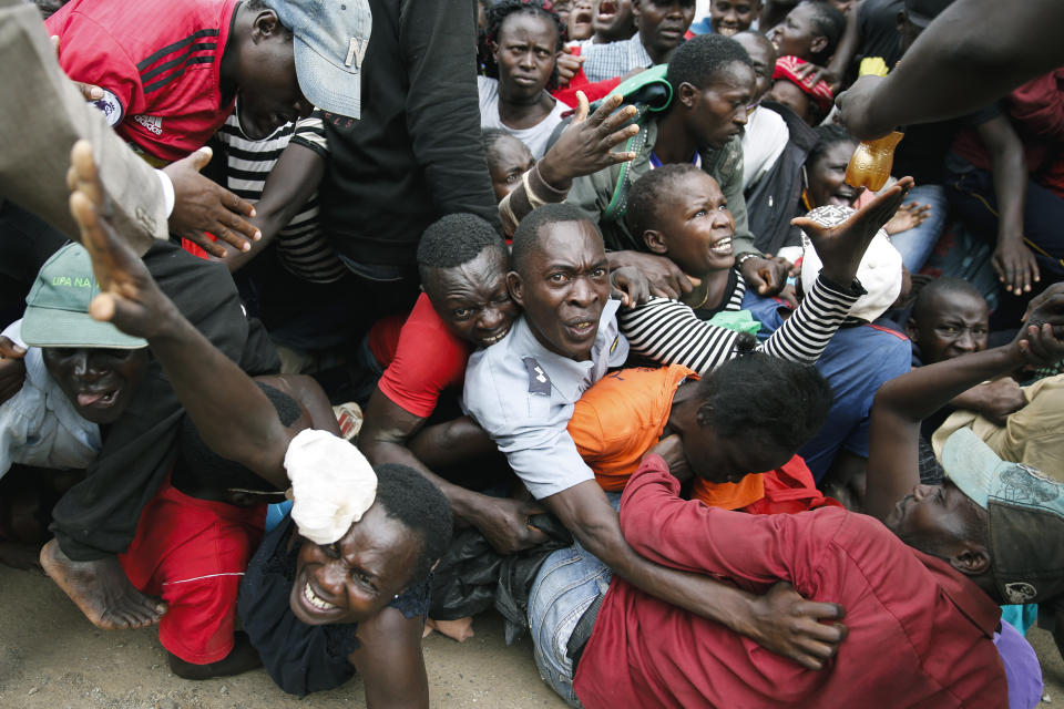 Residents desperate for a planned distribution of food for those suffering under Kenya's coronavirus-related movement restrictions push through a gate and create a stampede, causing police to fire tear gas and leaving several injured, at a district office in the Kibera slum, or informal settlement, of Nairobi, Kenya, Friday, April 10, 2020. (AP Photo/Brian Inganga)