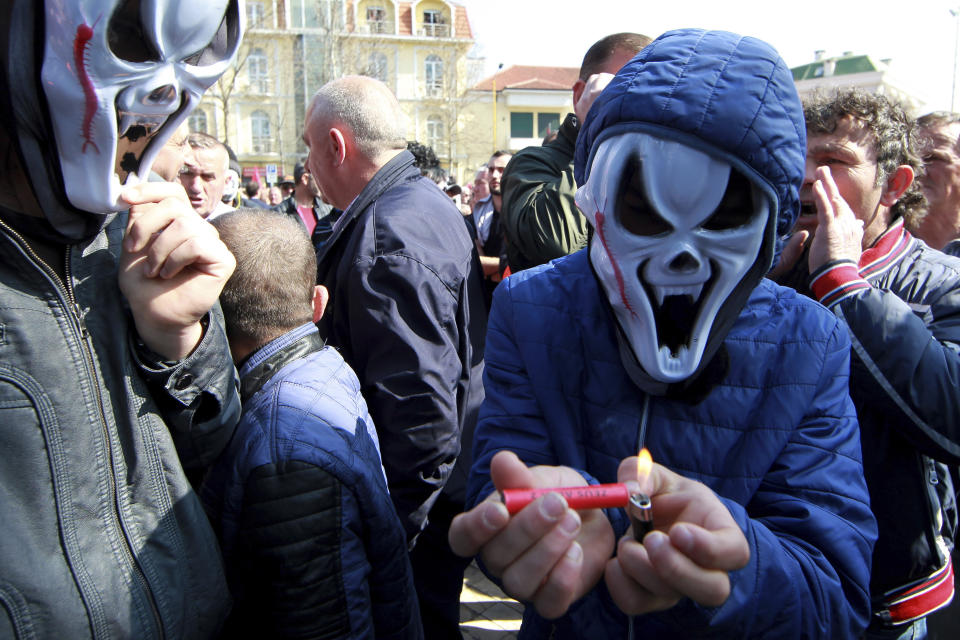 A protestor wearing in a mask lights a flare during an anti-government rally in Tirana, Albania, Thursday, March 21, 2019. Thousand opposition protesters have gathered in front of Albania's parliament building calling for the government's resignation and an early election. Rally is part of the center-right Democratic Party-led opposition's protests over the last month accusing the leftist Socialist Party government of Prime Minister Edi Rama of being corrupt and linked to organized crime. (AP Photo/ Hektor Pustina)