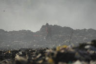 A man who scavenges recyclable materials for a living, walks past a mountain of garage amidst smoke from burning trash at Dandora, the largest garbage dump in the capital Nairobi, Kenya Wednesday, March 20, 2024. U.N. agencies have warned that electrical and electronic waste is piling up worldwide while recycling rates continue to remain low and are likely to fall even further. (AP Photo/Brian Inganga)