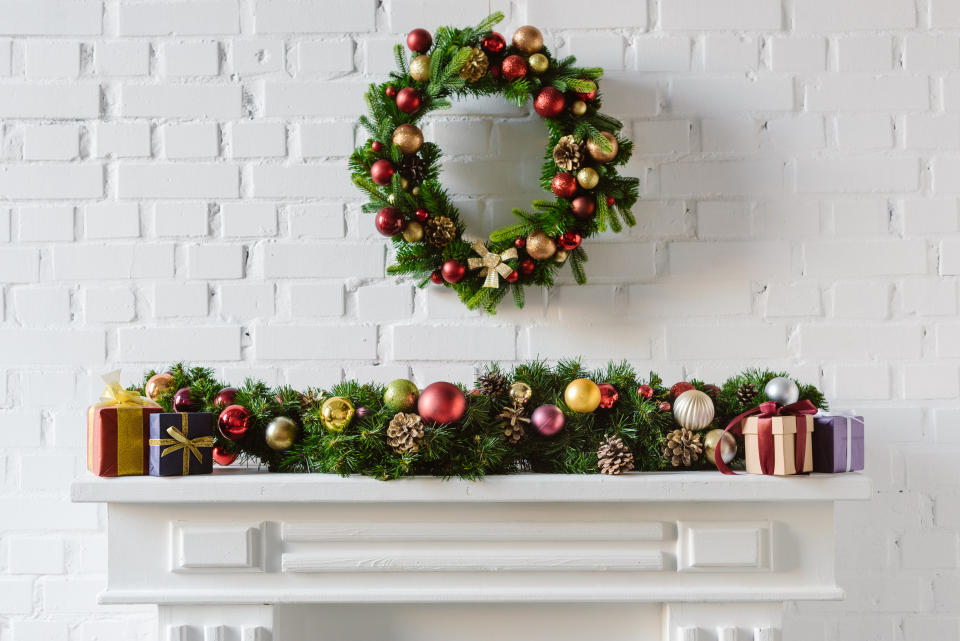 Christmas wreath and decorations over fireplace mantel with white brick wall. (Getty Images)