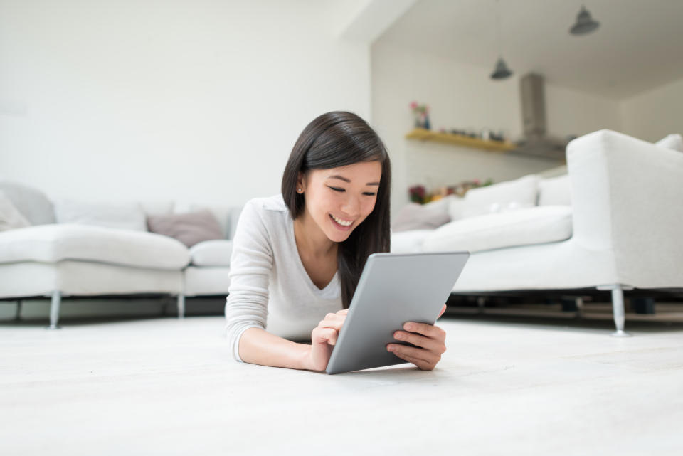 Happy Asian woman social networking on a tablet computer and relaxing at home