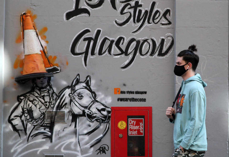 A member of the public wearing a face mask walks passed art work on a wall in Glasgow. (Photo by Andrew Milligan/PA Images via Getty Images)