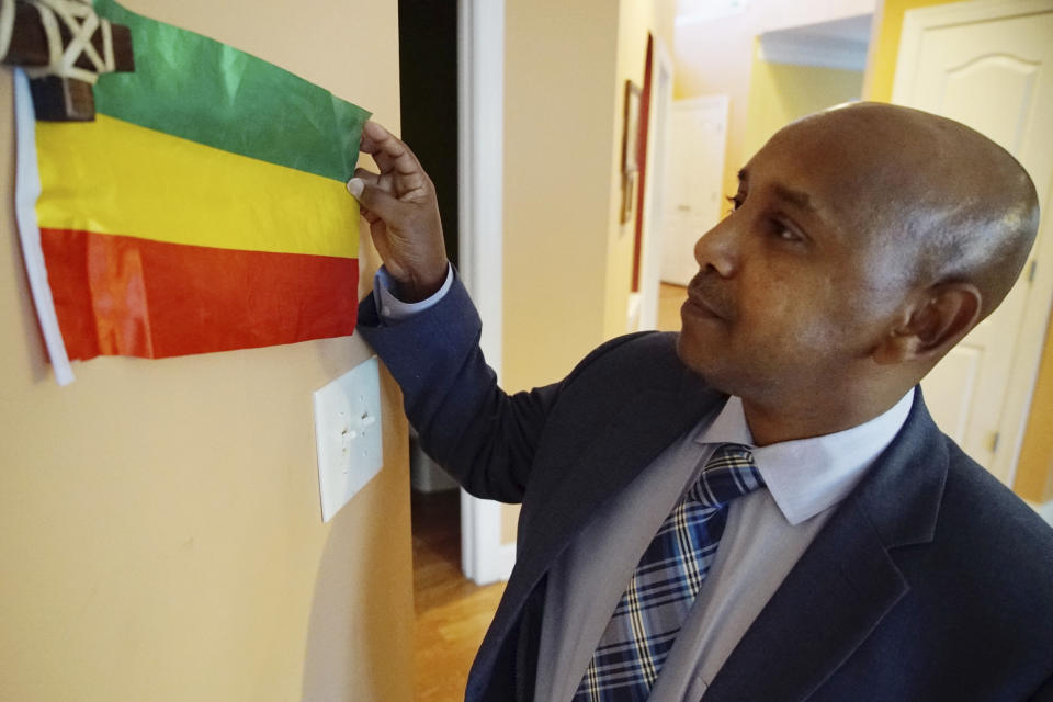 Tewodrose Tirfe stretches out a small Ethiopian flag displayed in the family room of his home in Harrisburg, N.C., on Thursday, Oct. 21, 2021. Tirfe is chairman of the Amhara Association of America, an advocacy group for Ethiopia's second-largest ethnic group. (AP Photo/Allen G. Breed)