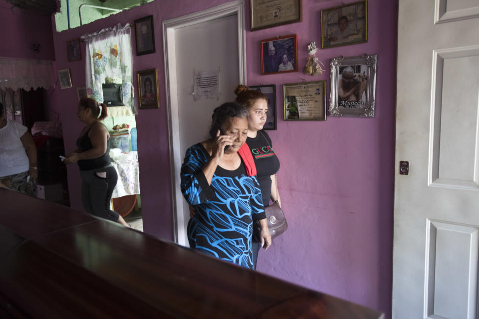 In this Oct. 31, 2018 photo, Haydee Esperanza Posadas talks on a mobile phone to a relative as she walks past the coffin that contains the remains of her son, Wilmer Gerardo Nunez, during a wake in her home in the Ciudad Planeta neighborhood of San Pedro Sula, Honduras. About 20 people came to the brief wake, where the coffin took up most of the living room. (AP Photo/Moises Castillo)