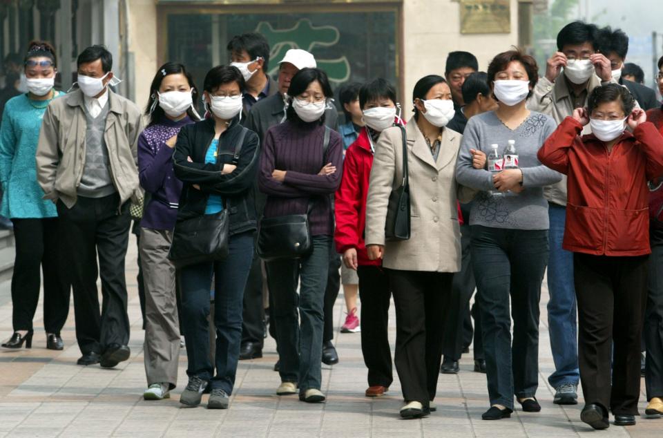 Chinese tourists all wearing masks walk down a commercial district in Beijing in a group Wednesday, April 23, 2003.