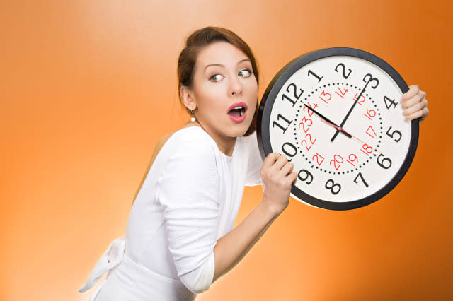 Closeup portrait woman, worker, holding clock looking anxiously, pressured by lack, running out of time, isolated orange backgro