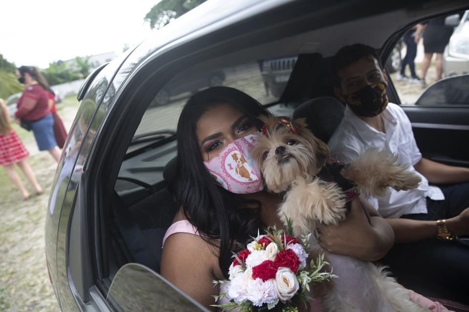 Wearing masks to prevent the spread of the new coronavirus, Erica da Conceicao and Joao Blank ride in the back seat of a car for a drive-thru wedding at the registry office in the neighborhood of Santa Cruz, Rio de Janeiro, Brazil, Thursday, May 28, 2020. A Brazilian notary public hovering outside the car presided over Thursday's ceremony. The drive-thru marriage wasn’t the romantic vision the Blanks had imagined, but it is one of few possibilities in the era of COVID-19. (AP Photo/Silvia Izquierdo)