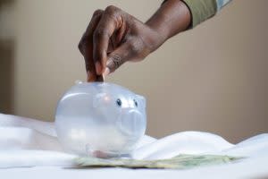 Black hand putting coins into a clear piggy bank