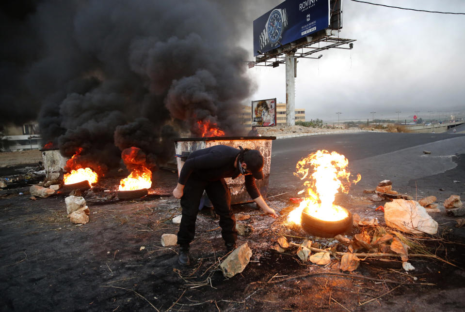 An anti-government protester burns tires, as they close the main highways during ongoing protests against the corruption and the Lebanese politicians, in Khaldeh, south of Beirut, Lebanon, Wednesday, Nov. 13, 2019. A local official for a Lebanese political party was shot dead by soldiers trying to open a road closed by protesters in southern Beirut late Tuesday, the army reported, marking the first death in 27 days of nationwide protests. (AP Photo/Hussein Malla)